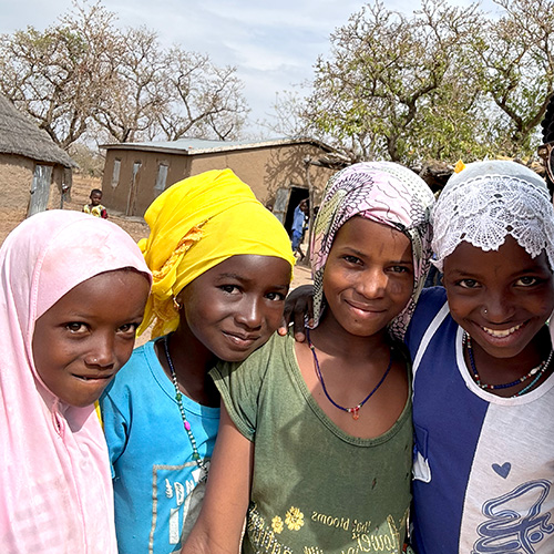 Three young Ghanaian girls wearing head coverings looking at the camera.