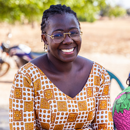 A woman smiling at the camera wearing a patterned orange blouse